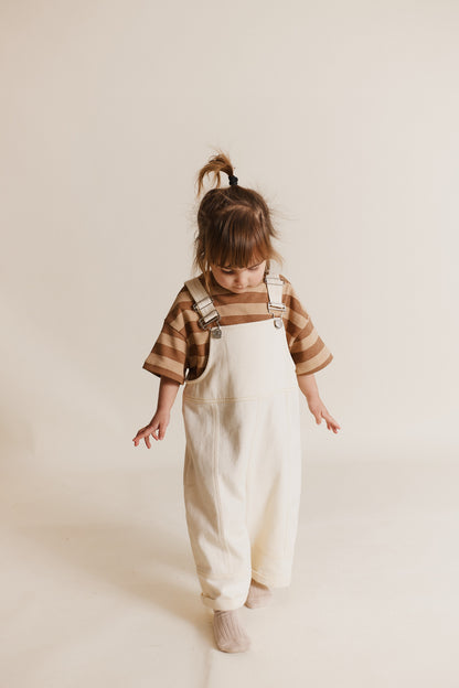 Stylish and comfortable kids' overalls in a cream color featuring a relaxed fit, adjustable straps, and durable organic cotton twill fabric. 