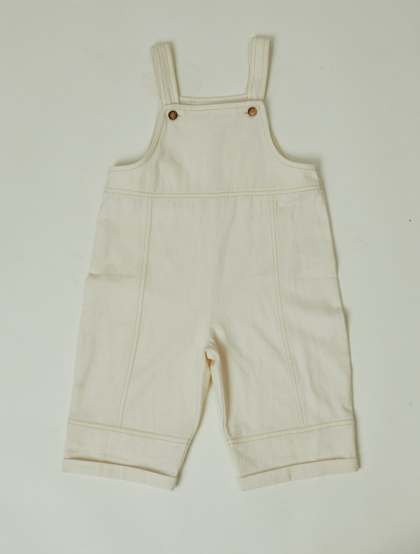 Stylish and comfortable kids' overalls in a cream color featuring a relaxed fit, adjustable straps, and durable organic cotton twill fabric. 