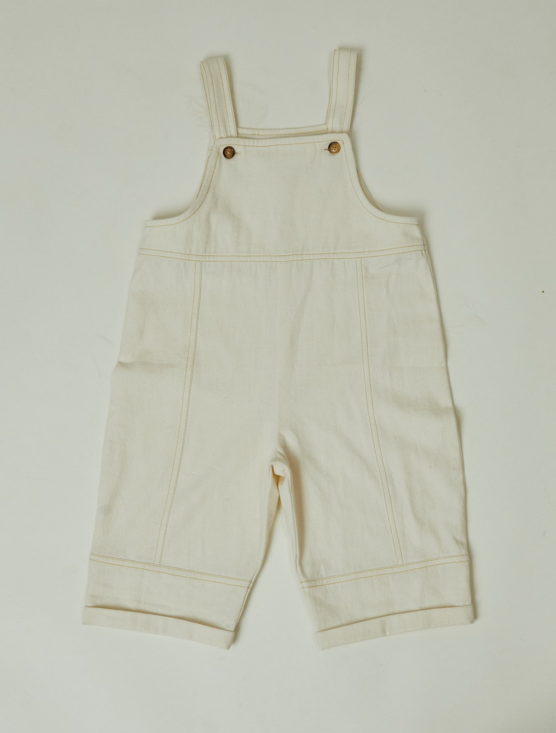 Stylish and comfortable kids' overalls in a cream color featuring a relaxed fit, adjustable straps, and durable organic cotton twill fabric. 