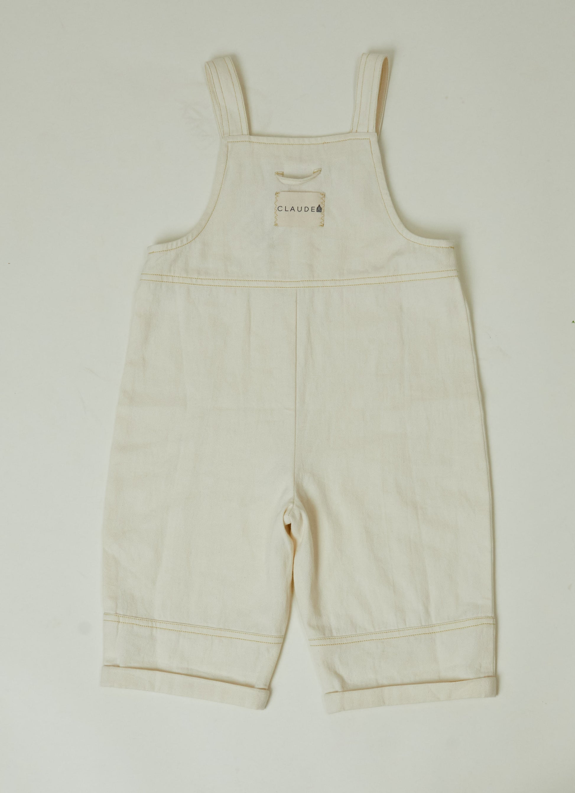 Stylish and comfortable kids' overalls in a cream color featuring a relaxed fit, adjustable straps, and durable organic cotton twill fabric. 